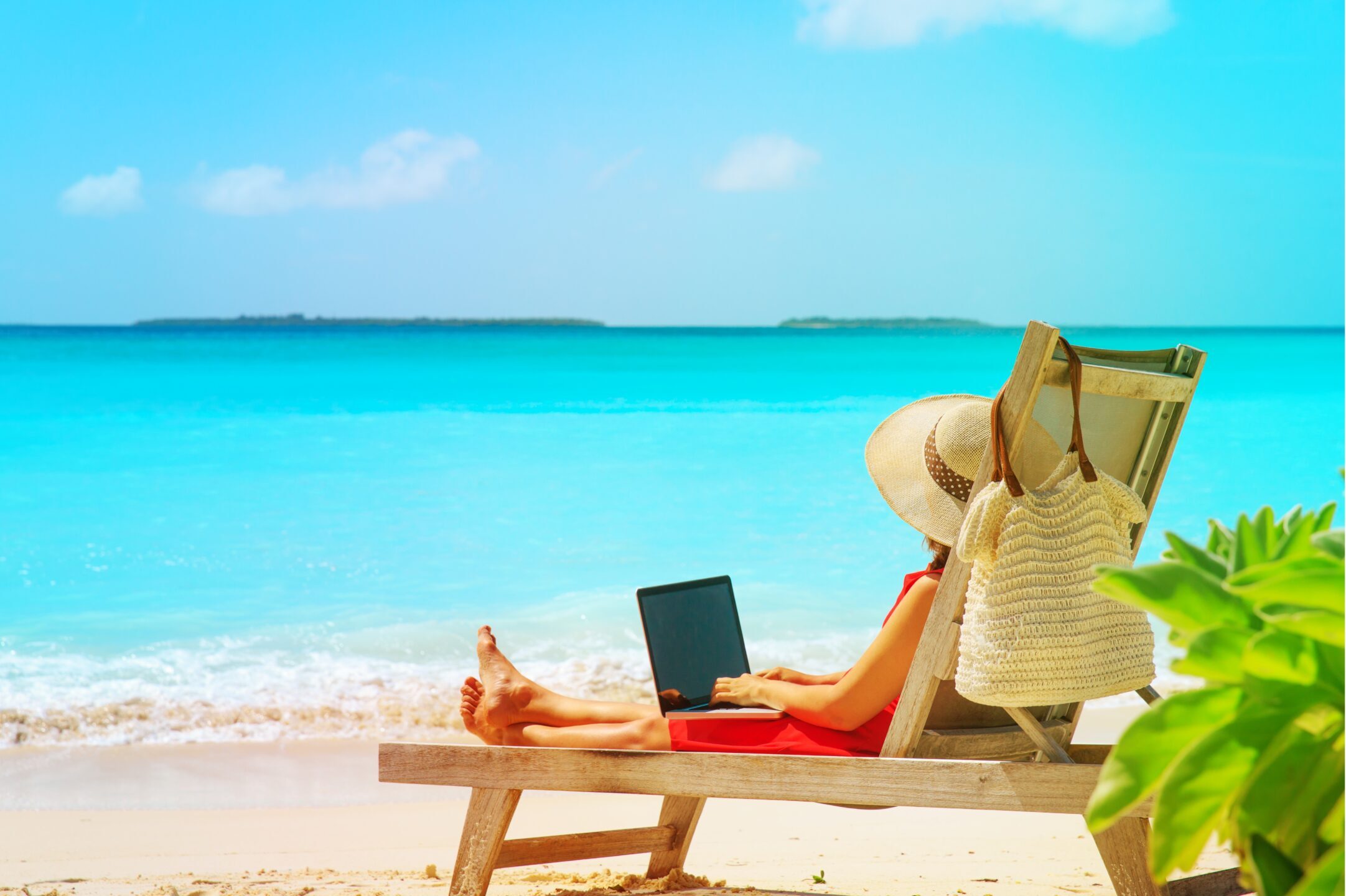 woman on a sun bed on a beach holding a laptop